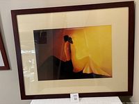 Framed print of two lovers in orange and yellow in wide dark brown frame with cream matting, hung and displayed showing entire piece.