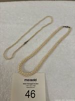 Two pearl necklaces laid on a light-colored surface. One single strand and one twisted double strand visible.