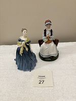 Two Royal Doulton figurines displayed on a white surface with number 27 card