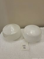 Two white glass schoolhouse style light shades displayed side by side on a white towel, showing comparative sizes and shapes.