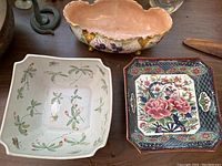 Top view of three shallow ceramic dishes: square strawberry-patterned, rectangular floral and fan patterned, oval grape cluster decorated bowl.