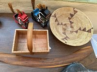 Painted wooden carvings, wood basket, woven basket, and boomerang on wooden surface next to tiled wall