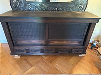 Front view of dark wood console table showing sliding doors with nailhead detail and five drawers at bottom