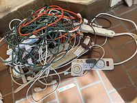 Photo of assorted extension cords, power strips, and timers tangled together on floor.