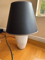 Full view of the gray ceramic lamp base with cracked pottery finish and attached black lampshade seen from the side on wooden floor.