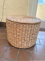 Side view of the large round woven basket with its lid on, showing the thick woven texture and tight construction.