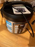 3 Squares multi cooker showing front digital control panel with preset buttons and instruction manual on top.