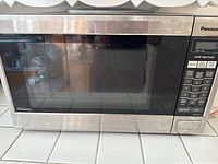 Front view of Panasonic microwave showing stainless steel door with black control panel on right side, and digital display.