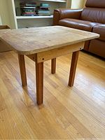 Side view of rough wooden side table showing worn surface, thick rectangular top, sturdy legs, and wooden supports.