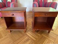 Front view of two midcentury wooden side tables showing drawers with wooden knobs and open storage compartments.