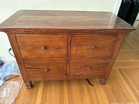 Front view of the dark wood dresser showing four drawers with wood knob handles and square legs.