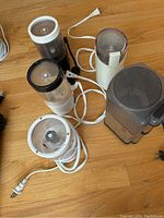 Five electric grinders arranged on a wooden floor, showing power cords and transparent grinding chambers with blades inside.