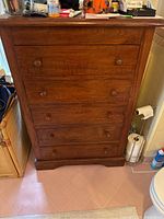 Front view of tall dark wood dresser showing five drawers with wood knob handles and scratches on surface.