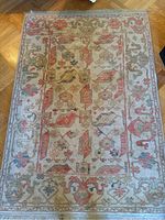 Full view of rectangular wool rug with intricate floral and geometric patterns in beige and pink colors on a wood floor.