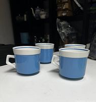 Four blue and white Mikasa coffee mugs arranged in an arc showing the exterior with white rims and mod handles