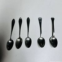 Five vintage silver teaspoons displayed side by side revealing slight difference in designs and handle shapes