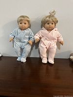 Two Bitty Baby Twin dolls in blue and pink pajamas displayed on a wooden surface.