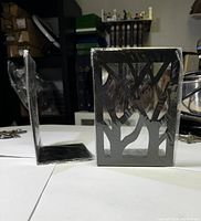 Two metal bookends shown separately and one pack sealed in plastic.