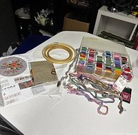 Complete embroidery starter kit items spread on a white table including wood hoops, colorful threads, printed fabric, and needle packs.