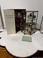 Complete set with gold hexagonal glass display case and all porcelain flower miniatures inside, accompanied by the original box and informational cards.