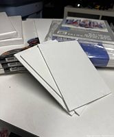 Multiple small and medium size white primed canvases, some shrink-wrapped in plastic, stacked on a white table in indoor setting.