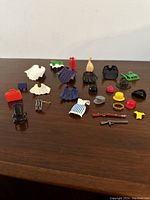 Various Playmobil accessories including hats, clothing pieces, weapons, a green cart vehicle, and other small props.