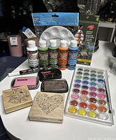 Overview of the art supplies including paints, paint palette, ink pads, stamps, and marker pen on a table.