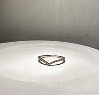 Front angled photo of thin rose gold plated ring shaped in a wishbone style with cubic zirconia stones lining the top.