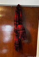 Red and black plaid scarf hanging, showing full length and fringe ends.
