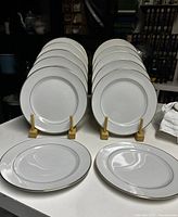 Set of 12 white Mikasa Doric salad plates with gold trim, displayed vertically in two groups of six and two plates laid flat on table