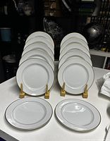 Group of twelve white plates with gold rim displayed on wooden stands