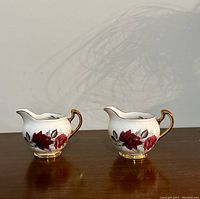Two Royal Imperial cream dishes with red rose patterns and gold handles on a wooden surface, front view showing the rose designs.