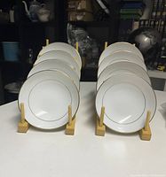 Eight Mikasa dessert bowls arranged in two sets of four on wooden stands, showing the gold rim and white base color.