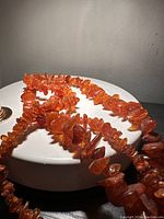Close-up image of vintage Baltic amber chip bead necklace, showing warm orange translucent beads of varied irregular shapes and sizes on a white rounded base.