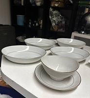 Four white serving bowls and one gravy boat with attached plate, all with gold trim, displayed on a white surface.