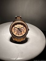 Front and slightly angled view of the vintage women's Fossil wristwatch with rose gold tone, crystal bezel, and multifunction dial on a white surface under lighting.