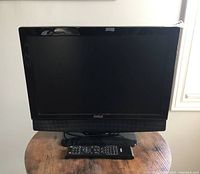 Front view of the Aveis 19 inch LCD TV on a wooden table with the remote placed in front.