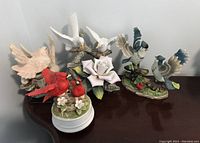 Four bird figurines on a surface, including the red cardinal musical figure and three ceramic birds with naturalistic painting and bases.