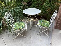 Full bistro set with table, two chairs and green leaf cushions in outdoor setting