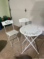 Front view of two white steel collapsible chairs and a round table in garage setting