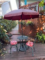 Full view of bistro set with two chairs, round table, and patio umbrella with red floral cushions on chairs