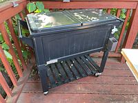 Full view of black Permasteel cooler cart with two lid compartments and lower shelf on a wooden deck.
