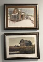 Two framed prints hanging on a wall, one above the other showing abandoned Victorian home on top and abandoned log cabin below.