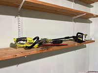 View of hedge trimmer and grass trimmer on wooden shelf