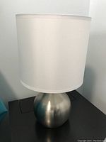 Photo showing one table lamp with chrome rounded metal base and white barrel shade.