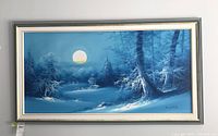 Full view of the framed winter landscape painting showing the snowy scene under a full moon signature at bottom right corner.