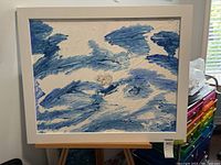 Frontal photo showing the artwork which features abstract blue and white brushstrokes on canvas in a white frame.