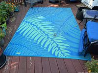 Full view of the outdoor carpet laid out on wooden deck showing blue background with light green fern design.