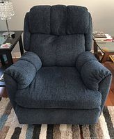 Front view of dark blue fabric recliner chair on area rug between two side tables