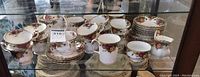 Wide view of shelves showing multiple teacups, saucers, coffee cups, plates, creamer and sugar bowl
